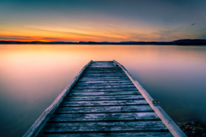 A serene wooden pier extending into a calm lake at sunset, with soft pastel colors in the sky reflecting on the water, symbolizing tranquility, mindfulness, and the journey of personal growth.